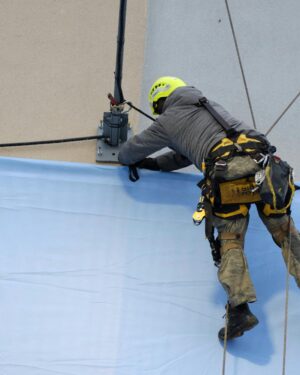 Rope access technician in safety gear fixes a large banner onto a building facade.