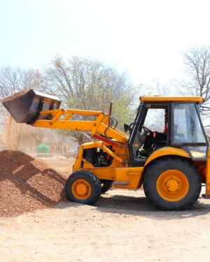 A yellow excavator moving gravel at an outdoor construction site during the day with clear skies.